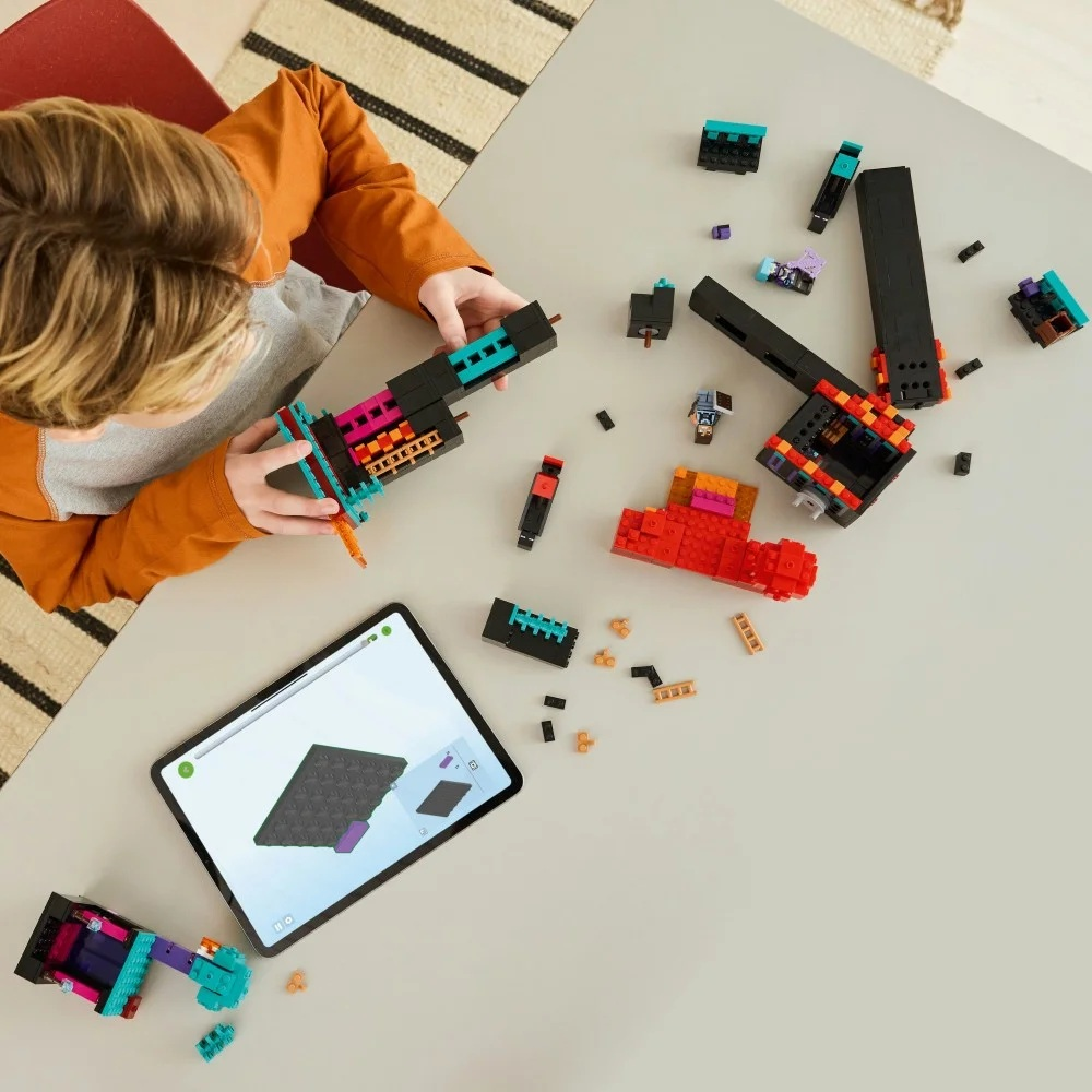 Dziecko buduje z kolorowych klocków, postępując zgodnie z instrukcjami na tablecie. Klocki i częściowo zbudowana konstrukcja leżą na stole.