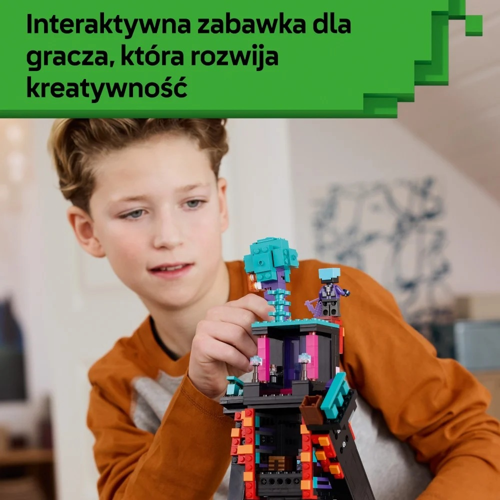 Chłopiec ogląda kolorową konstrukcję z klocków Lego. Konstrukcja to wieża z niebieskim dachem, a na górze stoi mała figurka.
