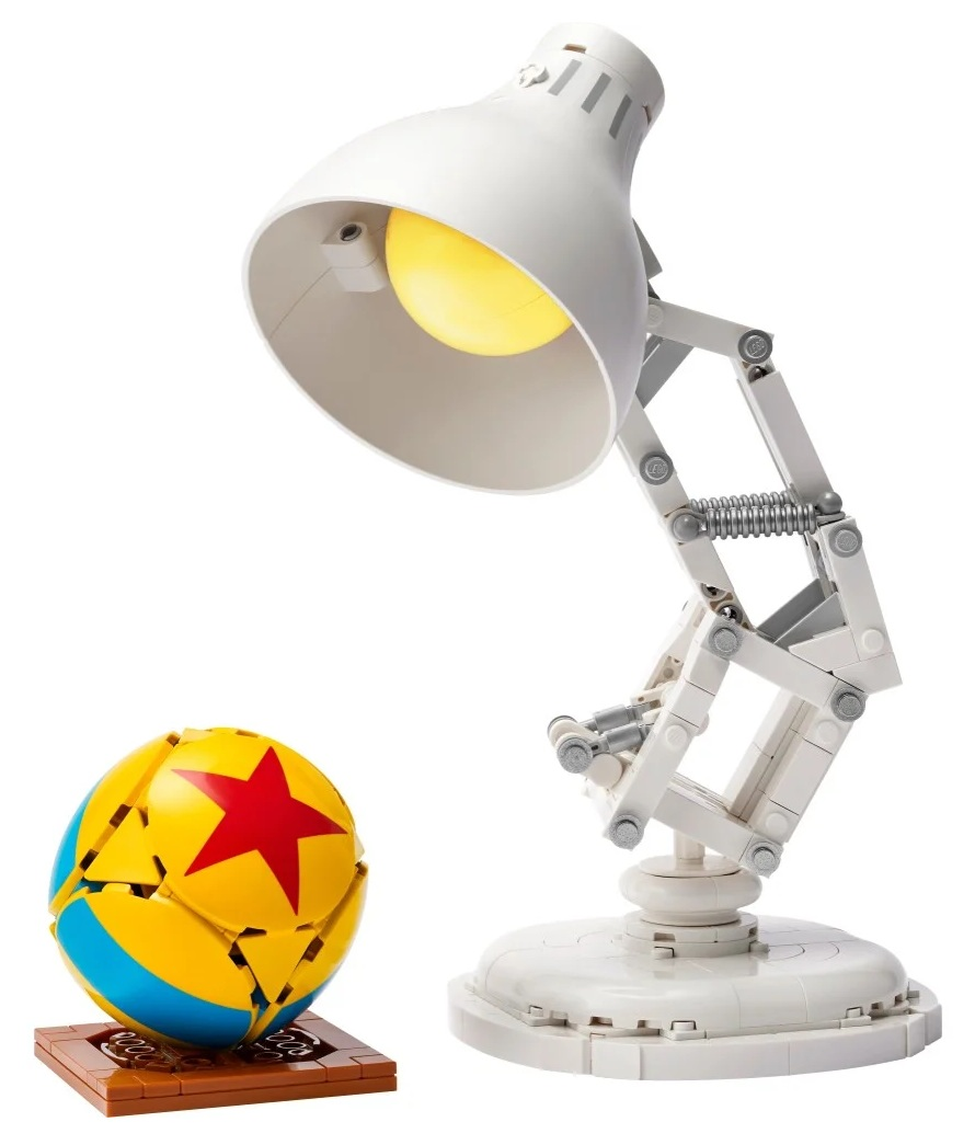 Biała lampa Lego z żółtą żarówką i żółtą, niebieską i czerwoną piłką na brązowej podstawie.