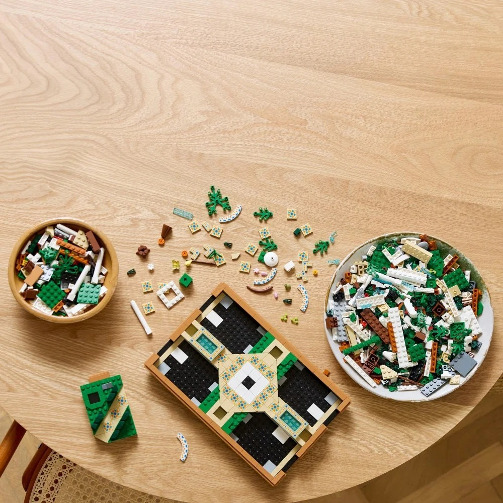 Drewniany stół z rozrzuconymi klockami Lego. Miski i talerz zawierają więcej klocków Lego. Konstrukcja Lego jest częściowo zmontowana.