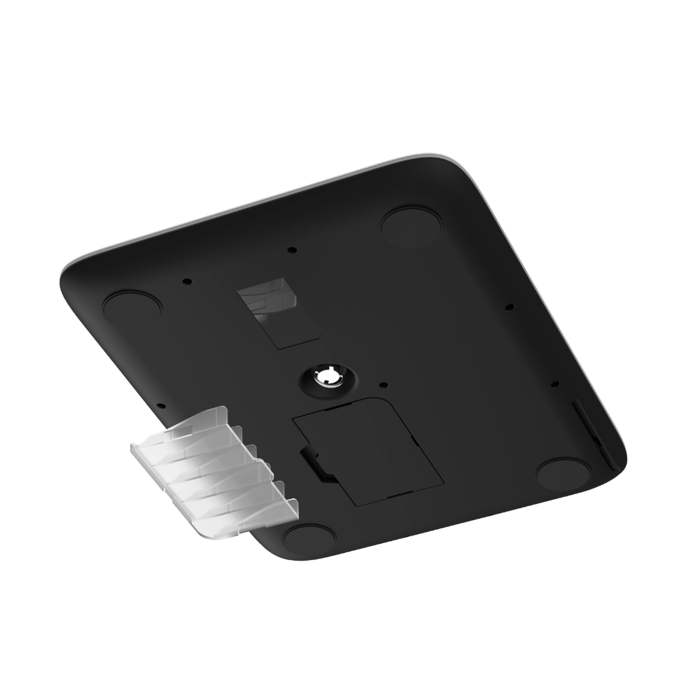 Spód czarnej wagi elektronicznej z białą obwódką. Posiada przezroczystą komorę baterii i cztery czarne nóżki.