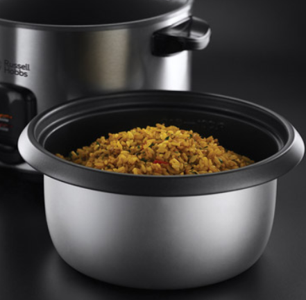 Garnek do ryżu ze stali nierdzewnej z ugotowanym żółtym ryżem w wewnętrznym garnku. Za nim stoi drugi garnek. Tło jest ciemne.