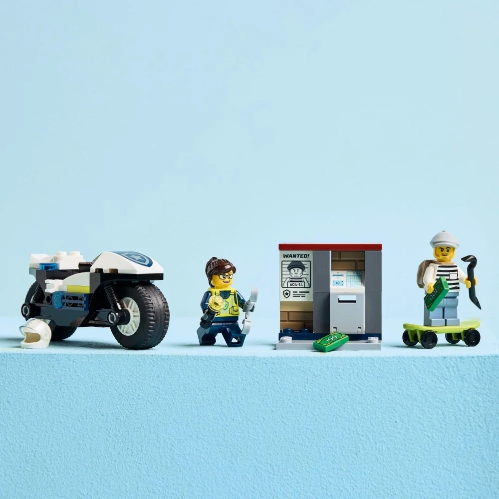 Scena Lego City: motocykl policyjny, policjant, bankomat z plakatem poszukiwawczym i złodziej na deskorolce. Są pieniądze.