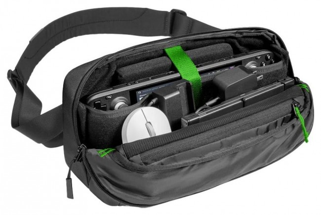 Otwarta czarna torba na ramię z urządzeniem do gier, ładowarką, myszą i akcesoriami. Widoczne zielone akcenty.
