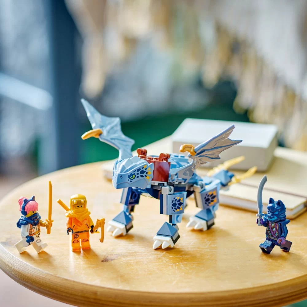 Zestaw Lego z niebieskim smokiem, trzema minifigurkami i akcesoriami. Na drewnianym stole z rozmytym tłem.