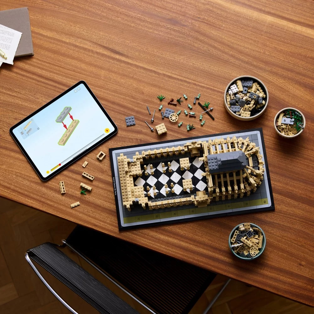 Model Lego budynku na stole. iPad pokazuje instrukcje. Klocki Lego rozrzucone wokół misek.