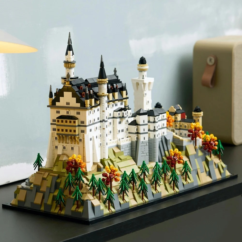 Model Lego zamku Neuschwanstein stoi na czarnej powierzchni. Jest biały z czarnymi dachami, otoczony drzewami i górami.