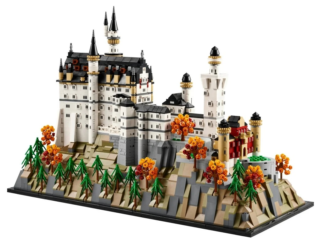 Model Lego białego zamku z czarnymi dachami i wieżami, osadzony na szarej skalisiej podstawie z drzewami.