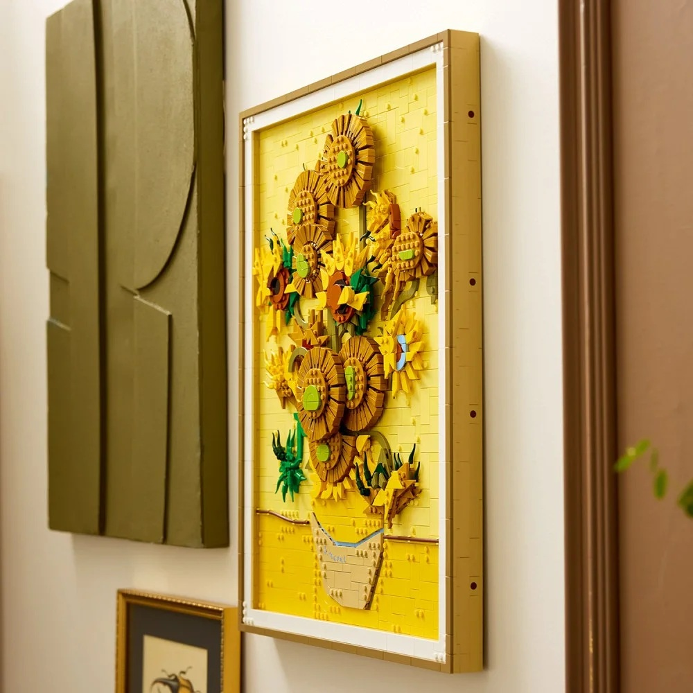 Dzieło sztuki Lego z słonecznikami Van Gogha w ramie. Inne dzieła sztuki są na ścianie. Kawałek jest żółty i brązowy.
