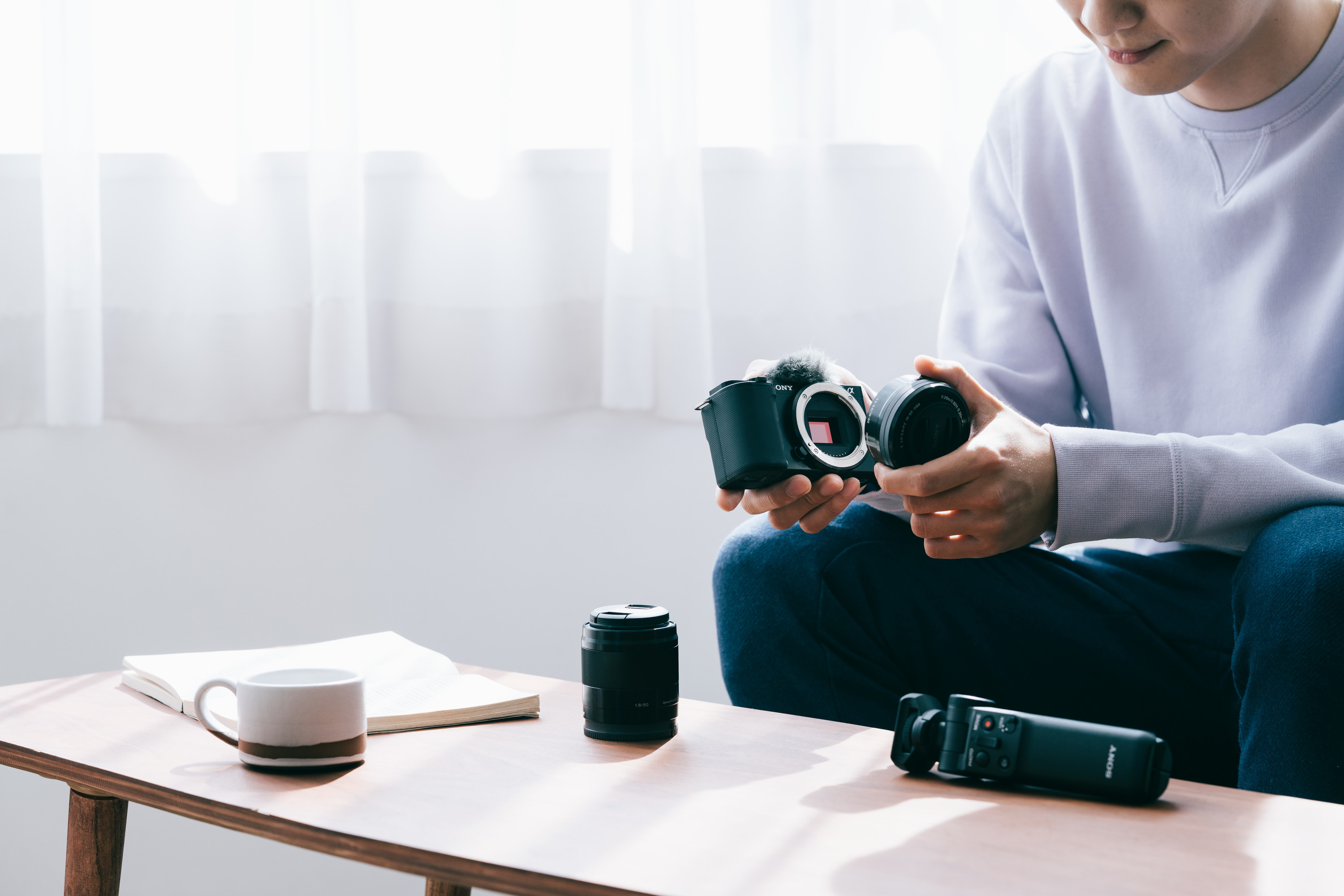 Une personne tient un appareil photo, fixant un objectif. Du matériel photo est sur une table.