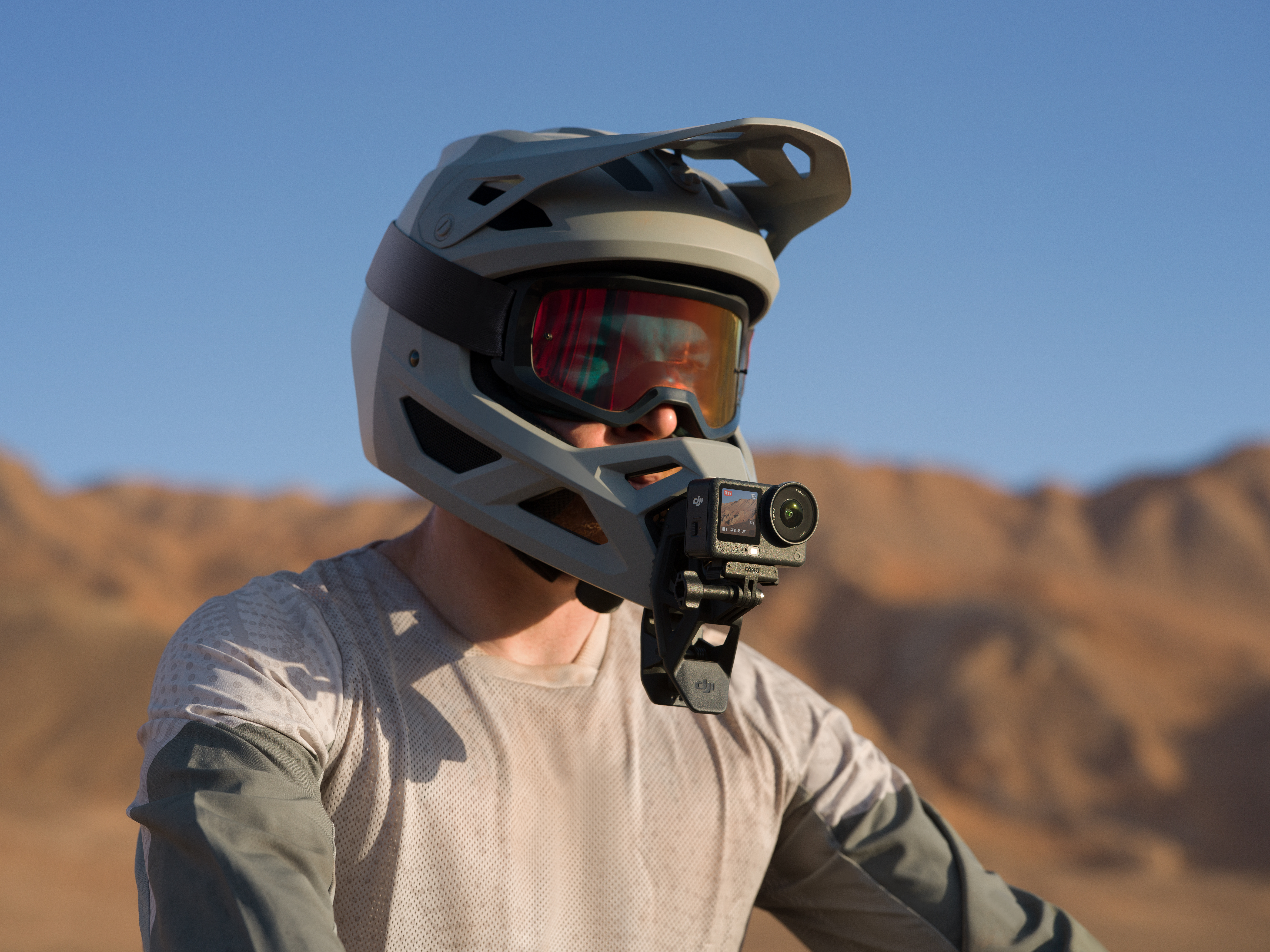 Osoba w kasku i goglach z dołączoną kamerą. W tle widać pasmo górskie i czyste niebo.