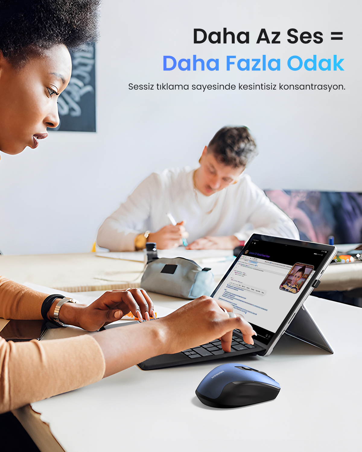 Bir kadın, klavye ve mavi fare ile bir tablet kullanıyor. Arka planda başka bir kişi var. Metin: Daha az sesle daha fazla odaklanma.