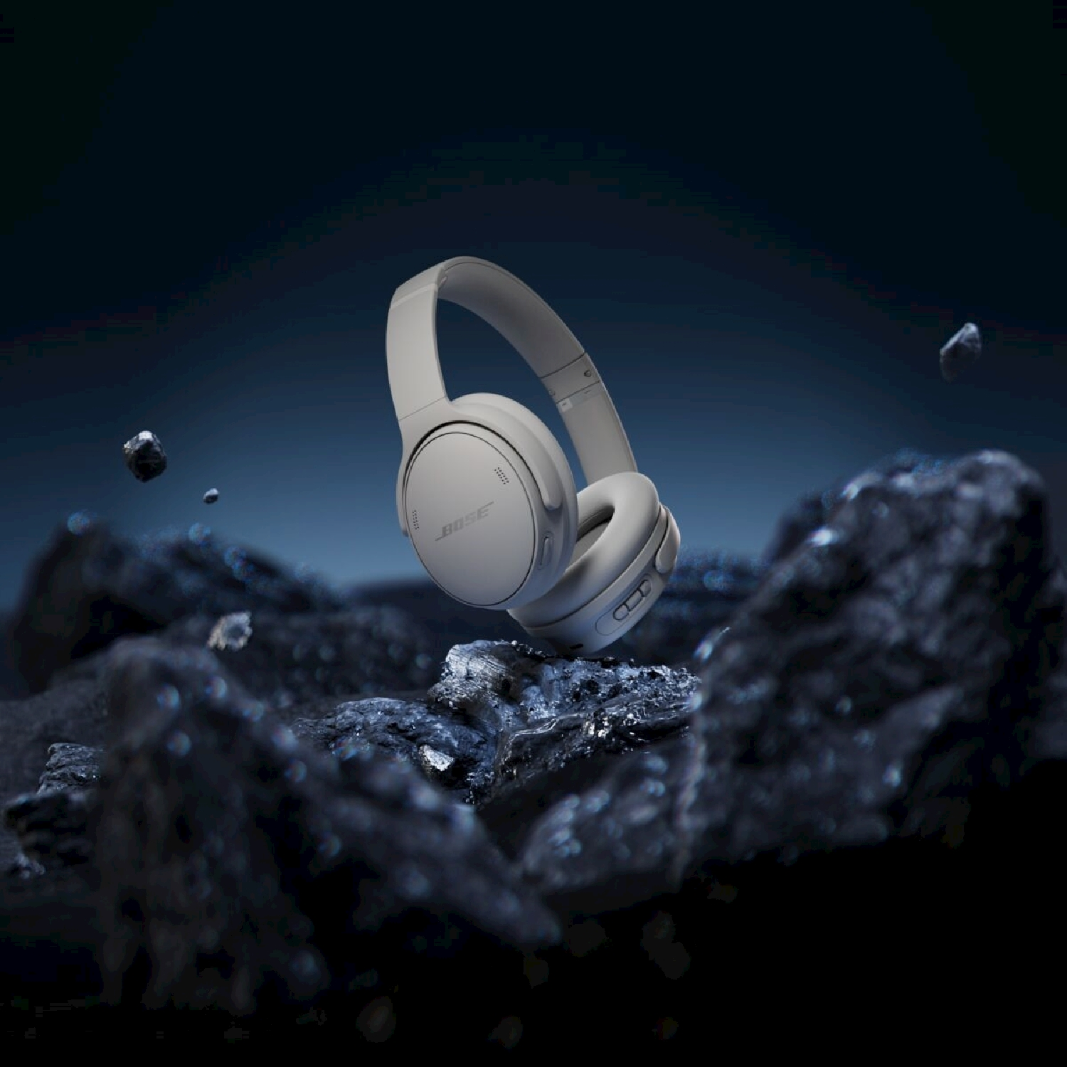 Cuffie Bose bianche levitano su terreno roccioso scuro. Sfondo blu scuro con rocce fluttuanti.