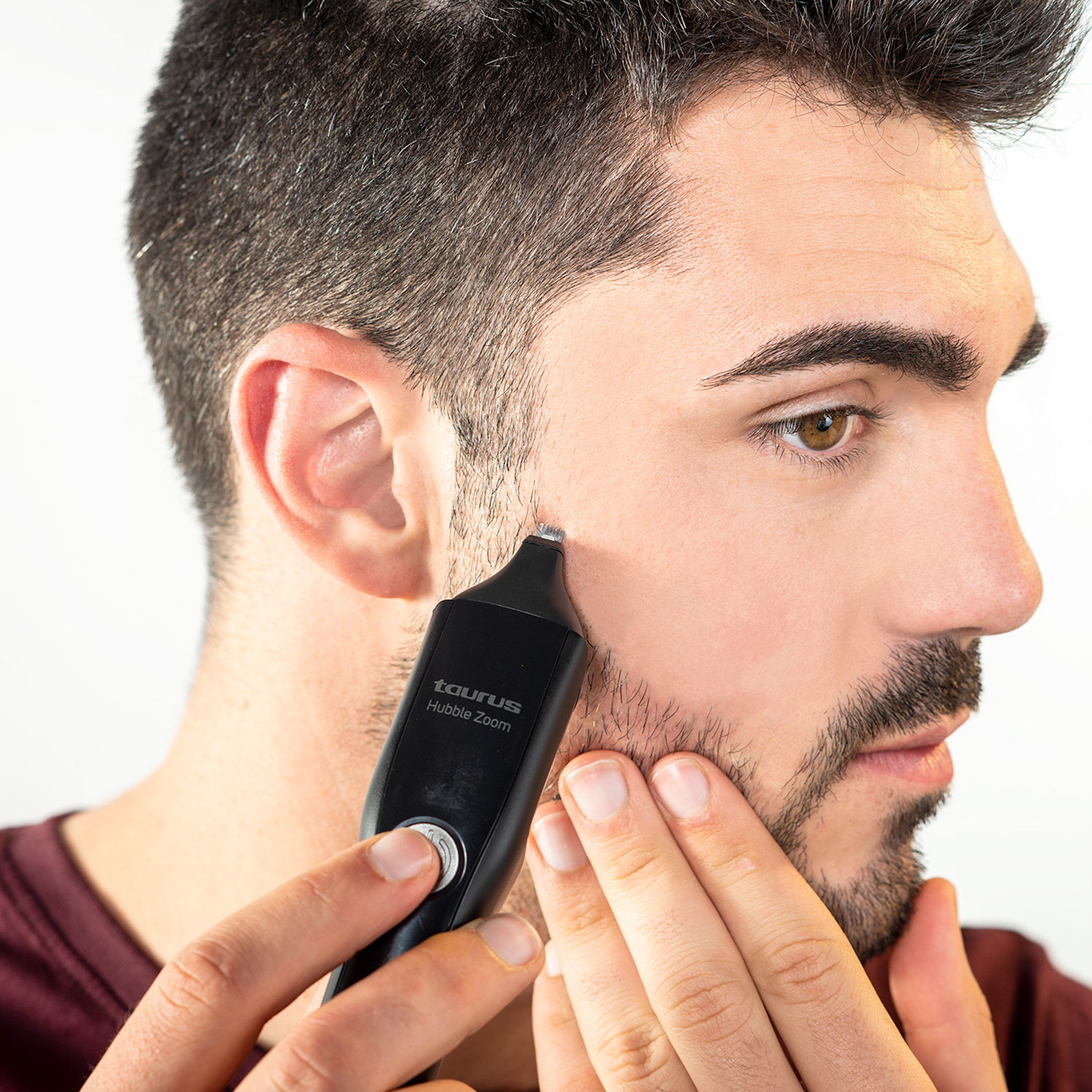 Un hombre se afeita la barba con una recortadora negra Taurus Hubble Zoom. Está de perfil, sosteniendo la recortadora en su mejilla.