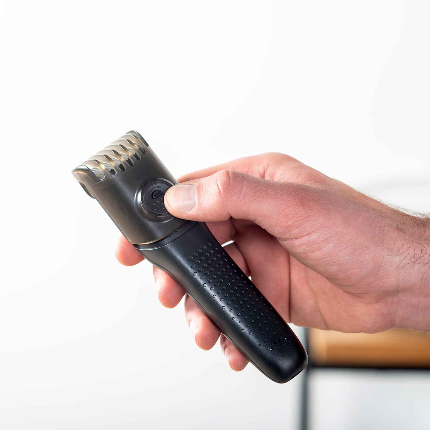 Una mano sostiene una recortadora de barba negra. La recortadora está enfocada, con fondo blanco. La mano sostiene la recortadora.