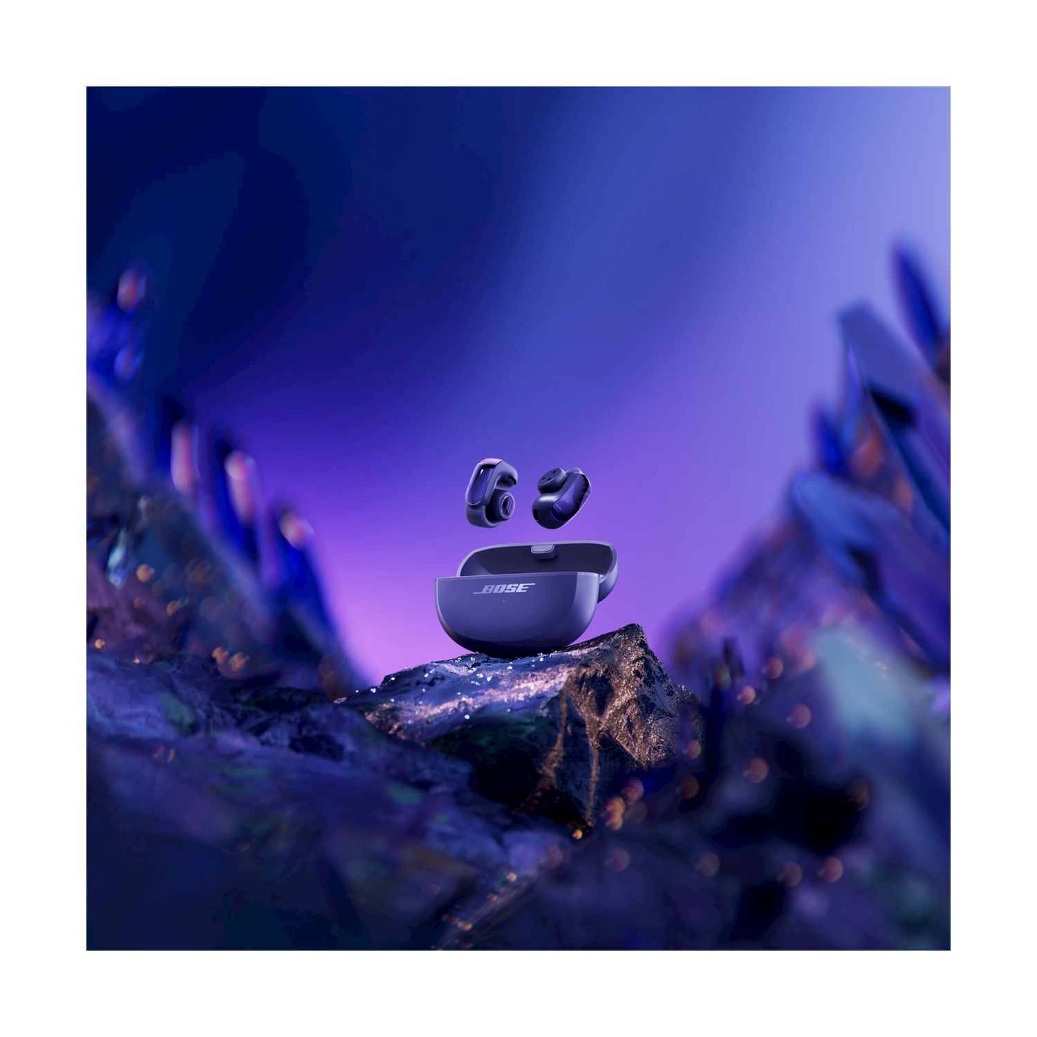 Auricolari wireless blu e custodia di ricarica su rocce, con sfondo blu-viola. Il marchio 'Bose' è visibile.