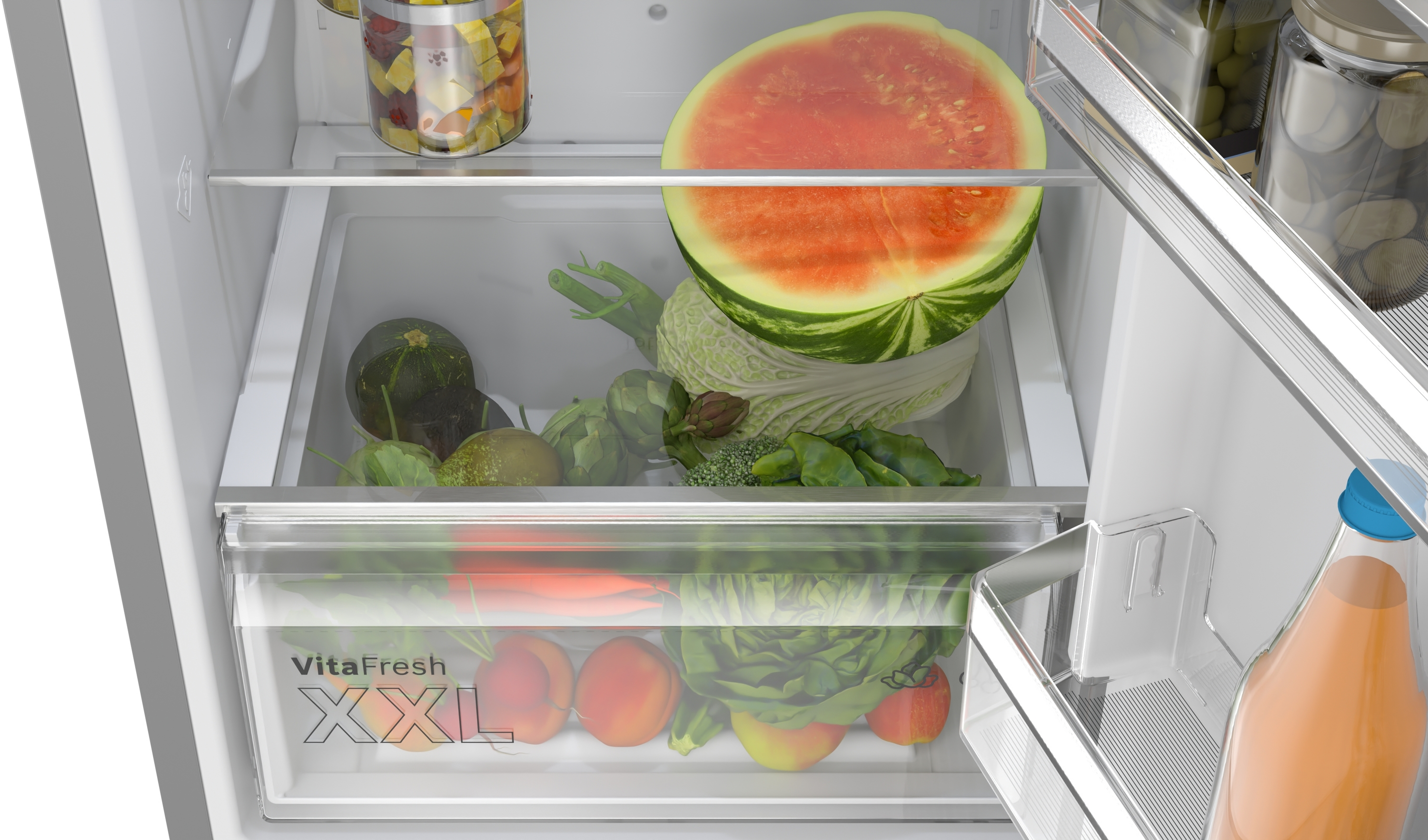 Im Kühlschrank sind Wassermelone, Gemüse und Obst auf Regalen und in Schubladen gelagert. Eine Flasche Saft ist sichtbar.