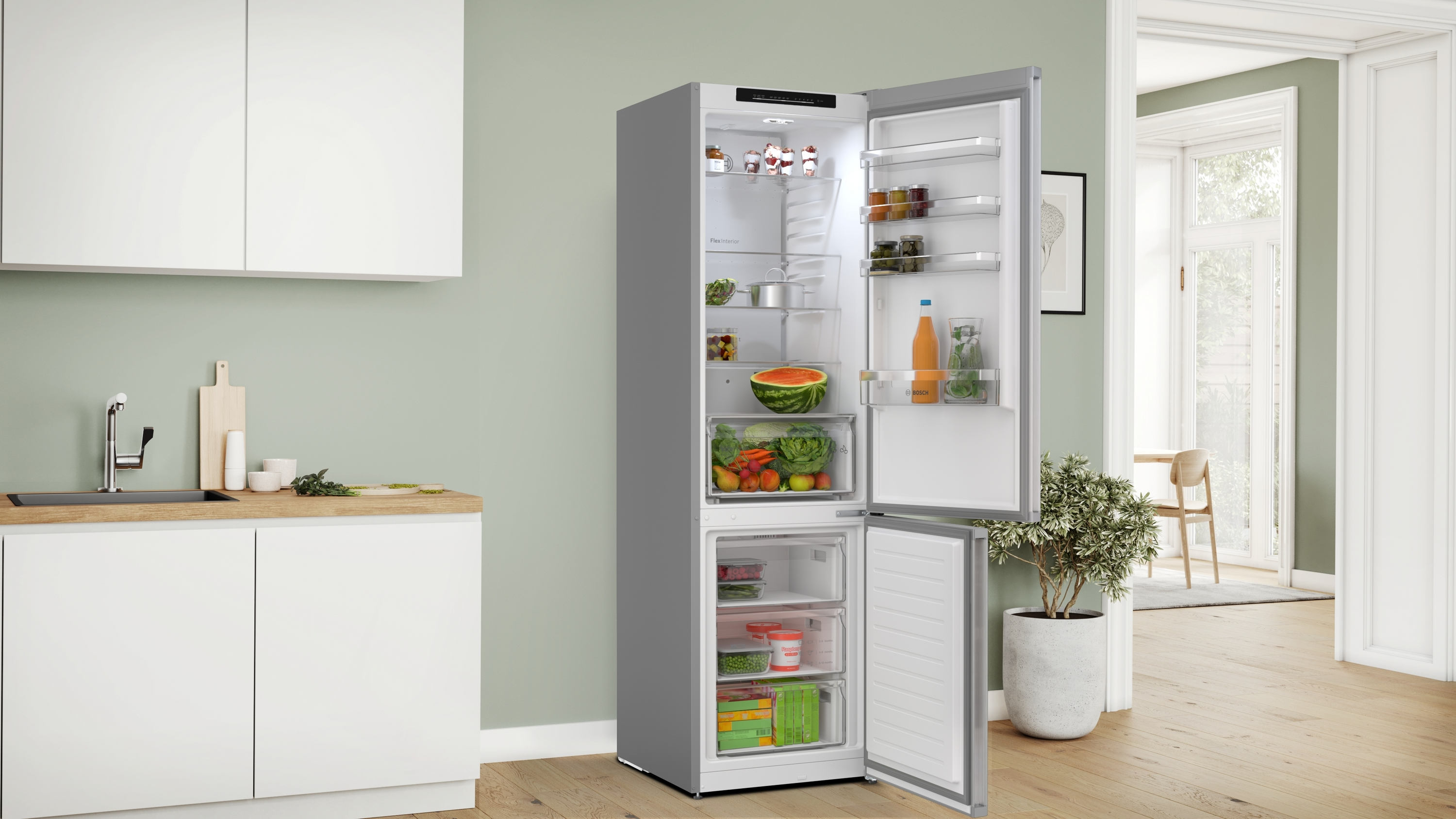 Offener Kühlschrank mit Lebensmitteln: Wassermelone, Gemüse, Obst und Getränke. Küche mit weißen Schränken und einer Pflanze.