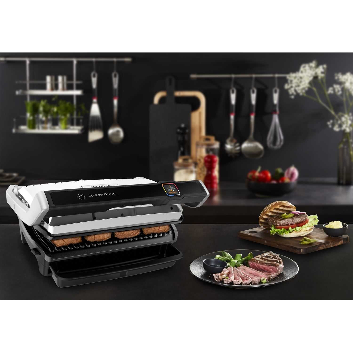 Un OptiGrill XL grillant des burgers et du steak. Un burger et un steak sont prêts sur une planche et une assiette, respectivement.