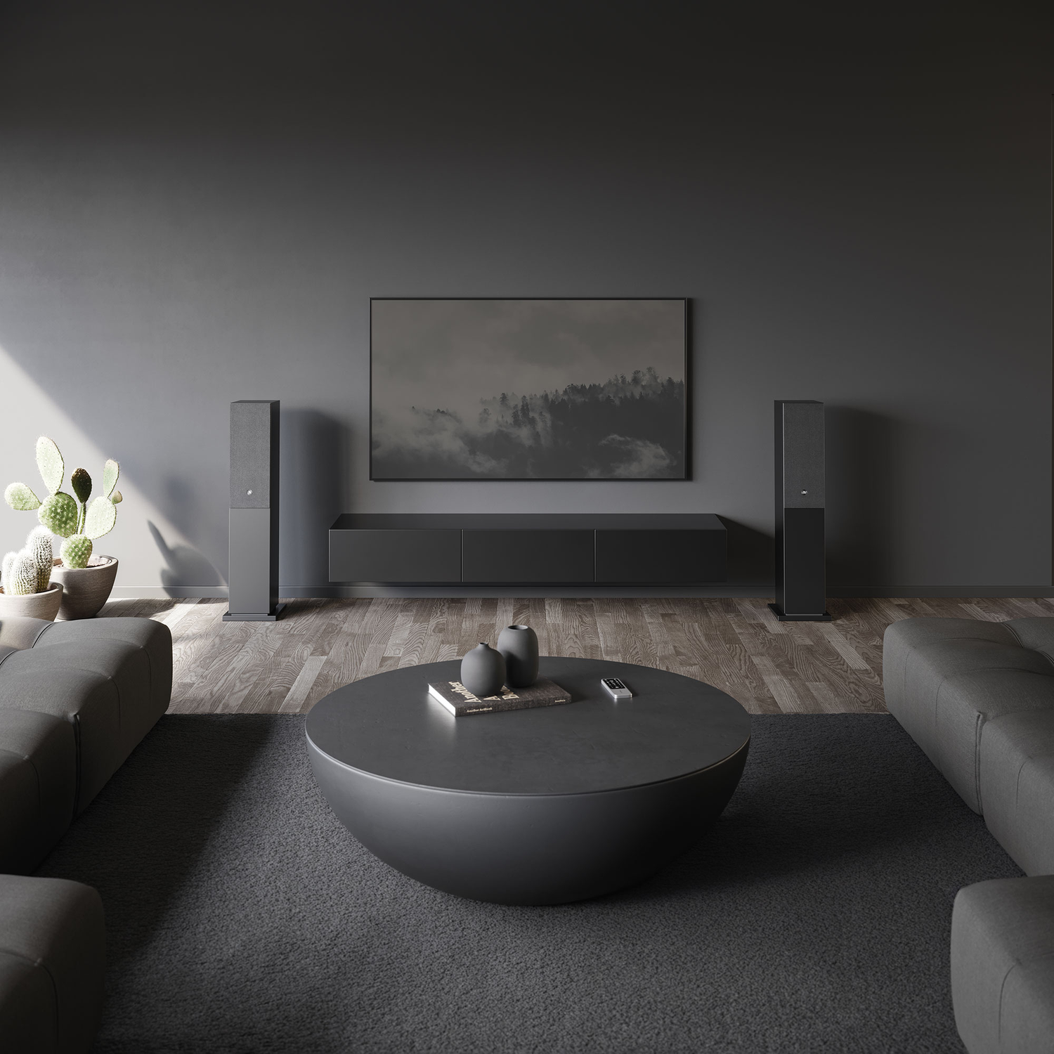 A modern living room with gray walls, sofa, and a round black coffee table. There's a TV, speakers, and a cactus.