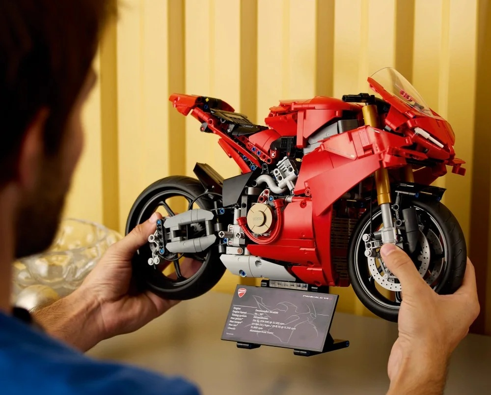 Osoba trzyma czerwony model motocykla Ducati. Model jest szczegółowy, z czarnymi kołami, złotymi widelcami i przezroczystą szybą.