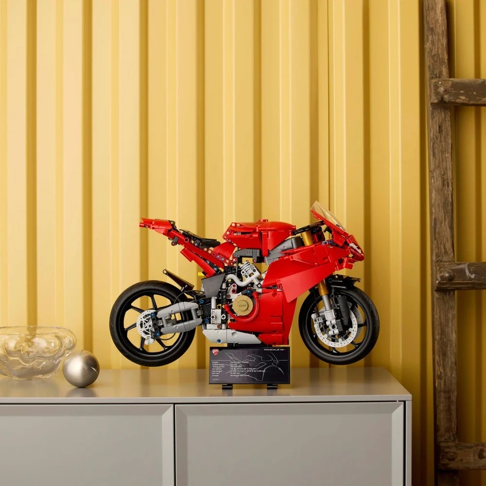 Czerwony model motocykla Ducati Lego stoi na szarej powierzchni. Żółta ściana jest w tle z drewnianą drabiną.