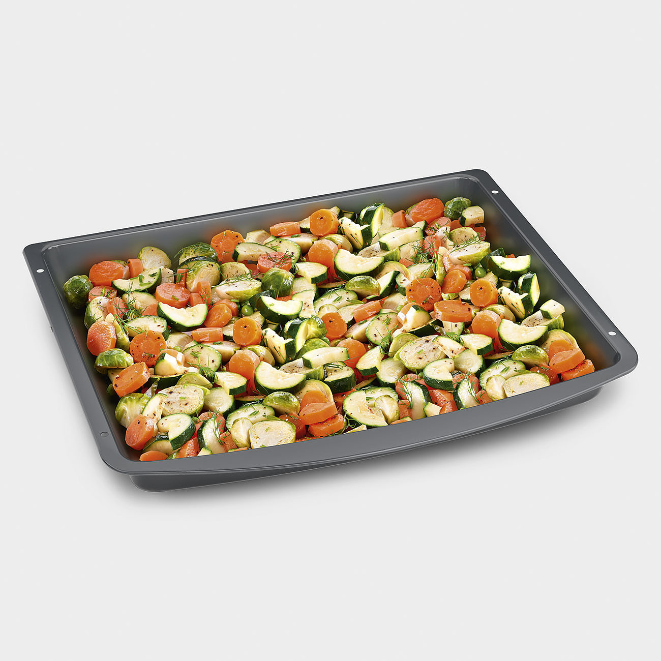 Geröstetes Gemüse in einem dunkelgrauen Backblech. Enthält Karotten, Zucchini und Rosenkohl. Weißer Hintergrund.