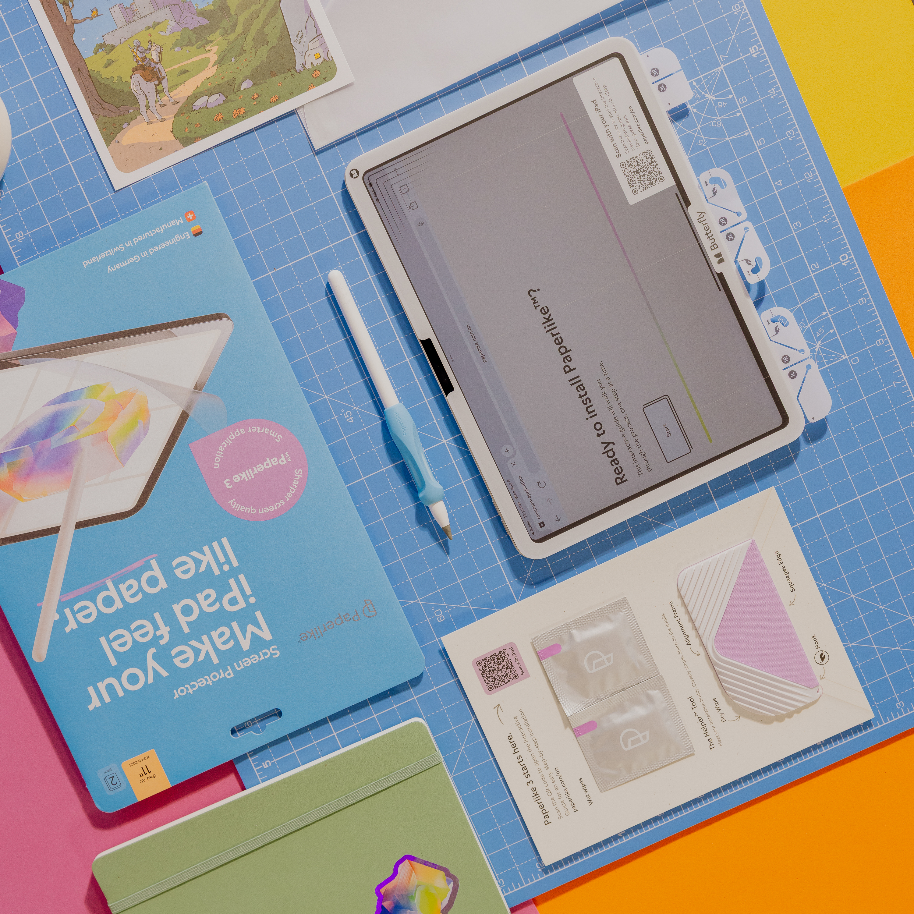 Ein iPad mit Displayschutz, Stift und Zubehör auf einer blauen Schneidematte. Inklusive Verpackung und Aufklebern.