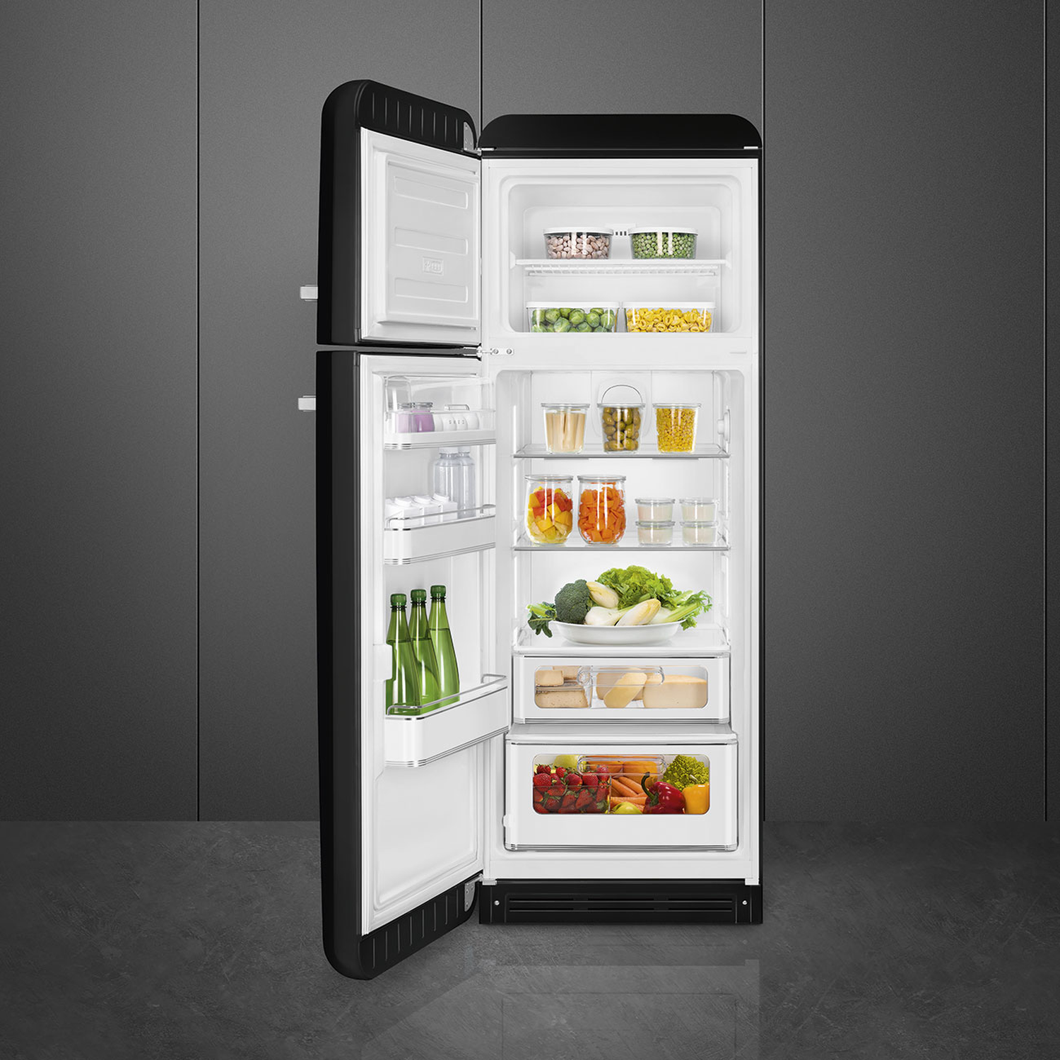 Open black refrigerator filled with food: vegetables, fruits, jars. Background is a gray wall.