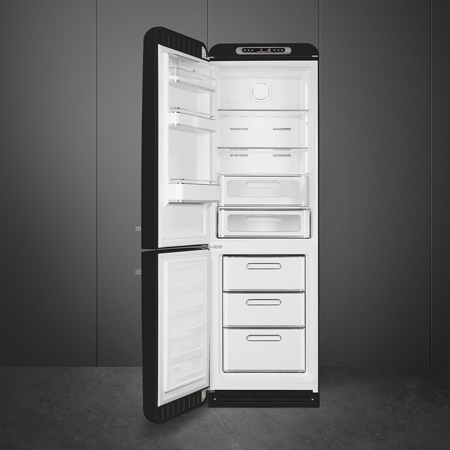 Open zwarte koelkast met wit interieur. Planken, lades en compartimenten zijn zichtbaar. Grijze muur op de achtergrond.