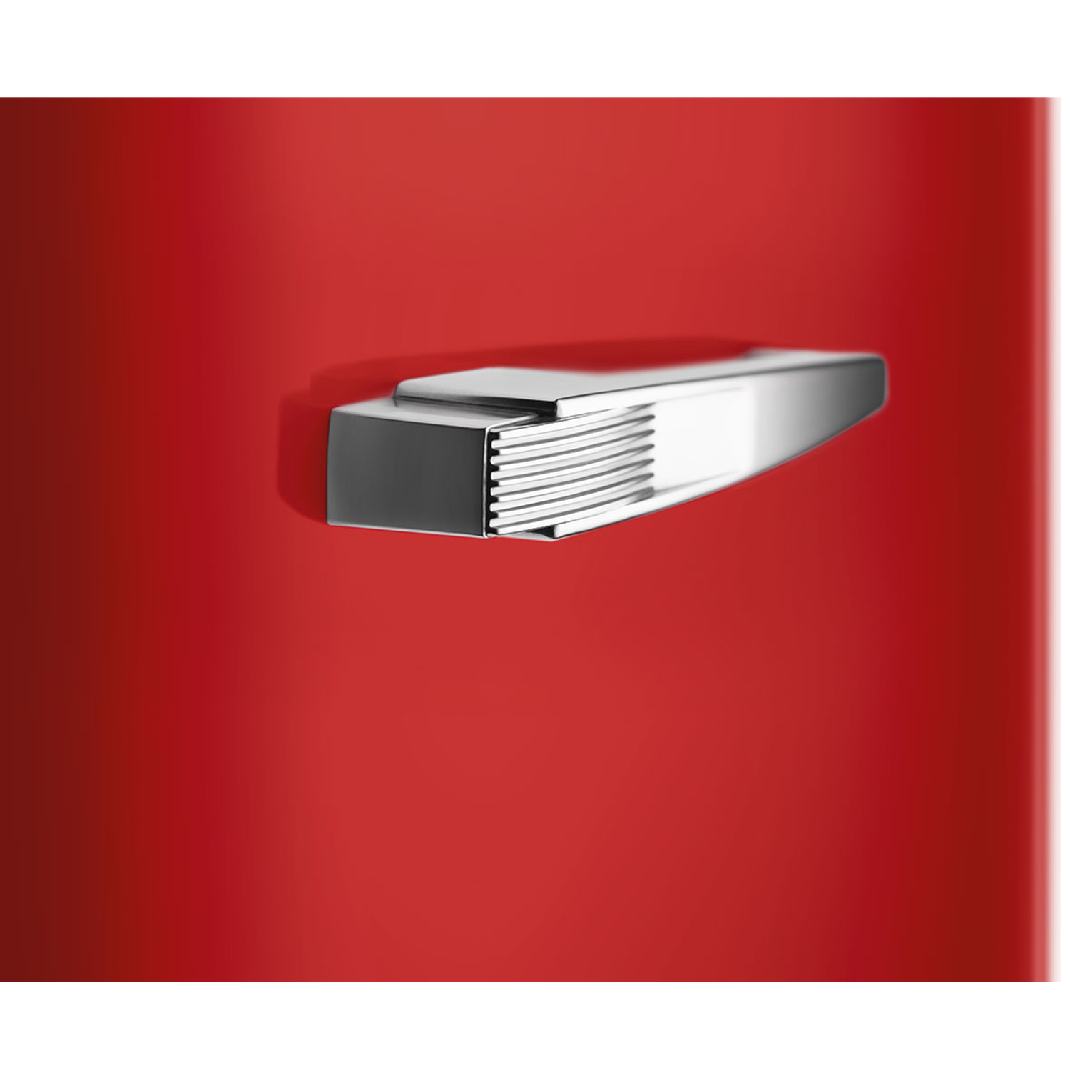 Close-up van een rood oppervlak met een glanzende zilveren handgreep. De handgreep heeft een rechthoekige basis en een gebogen, geribbelde bovenkant.