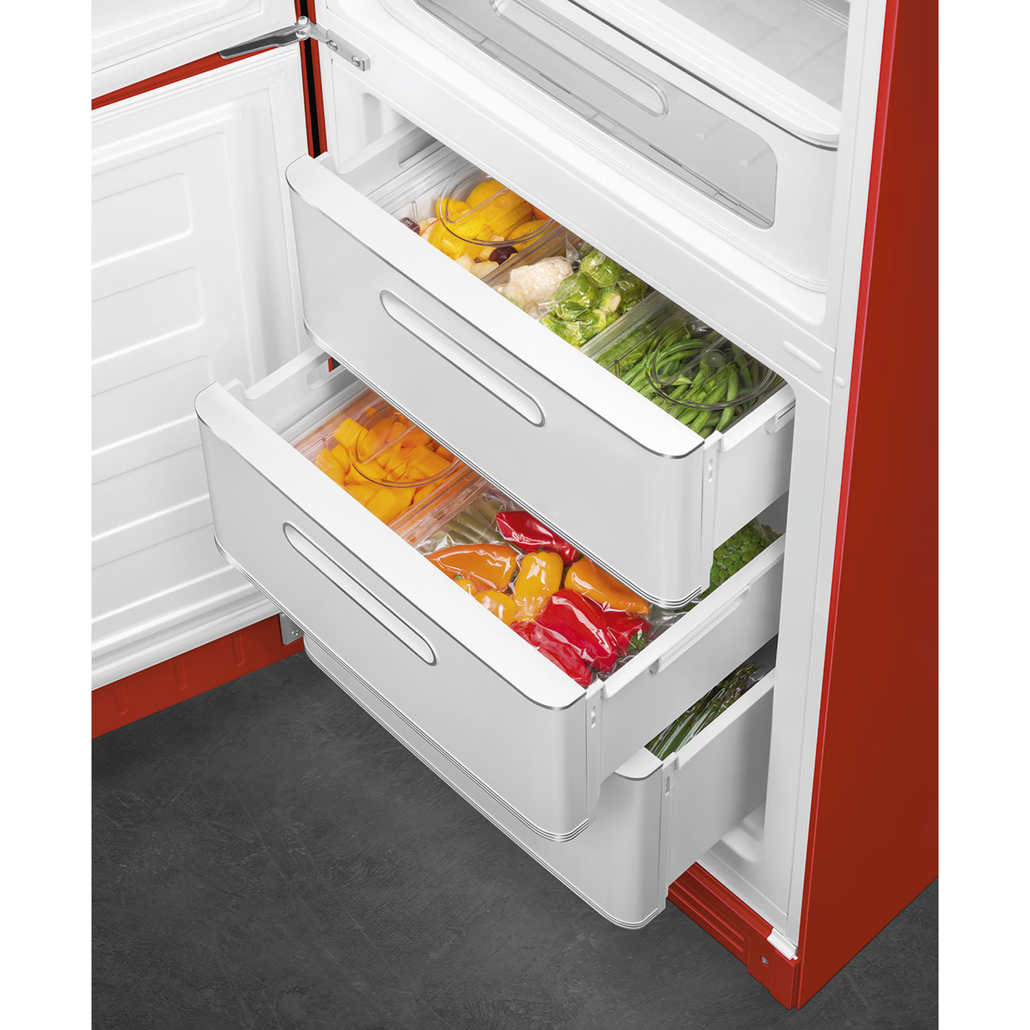 Open red refrigerator with vegetable-filled drawers. Bell peppers, green beans, and other produce are visible. White drawers.
