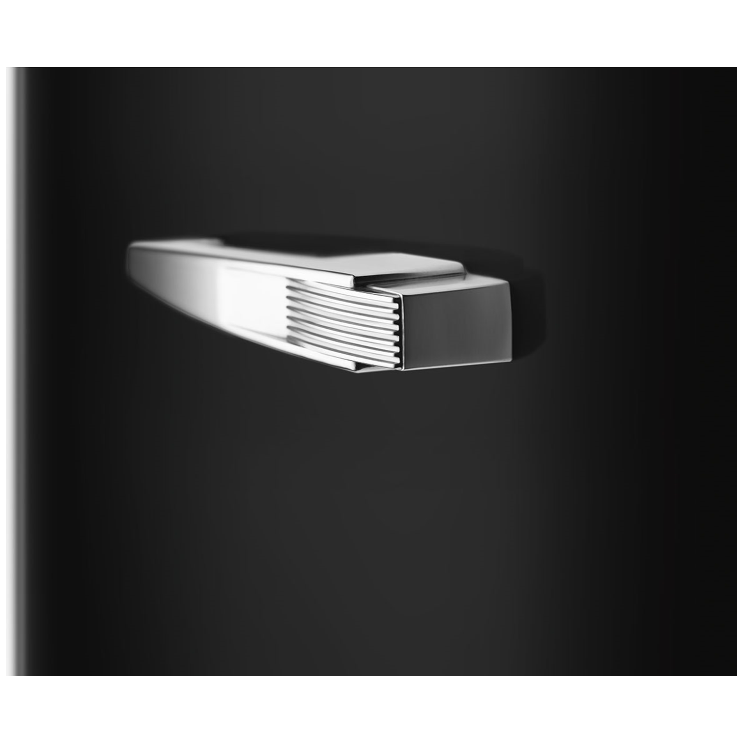 A close-up of a shiny, metallic object against a dark background. The object is rectangular with ridged edges. The background is black.