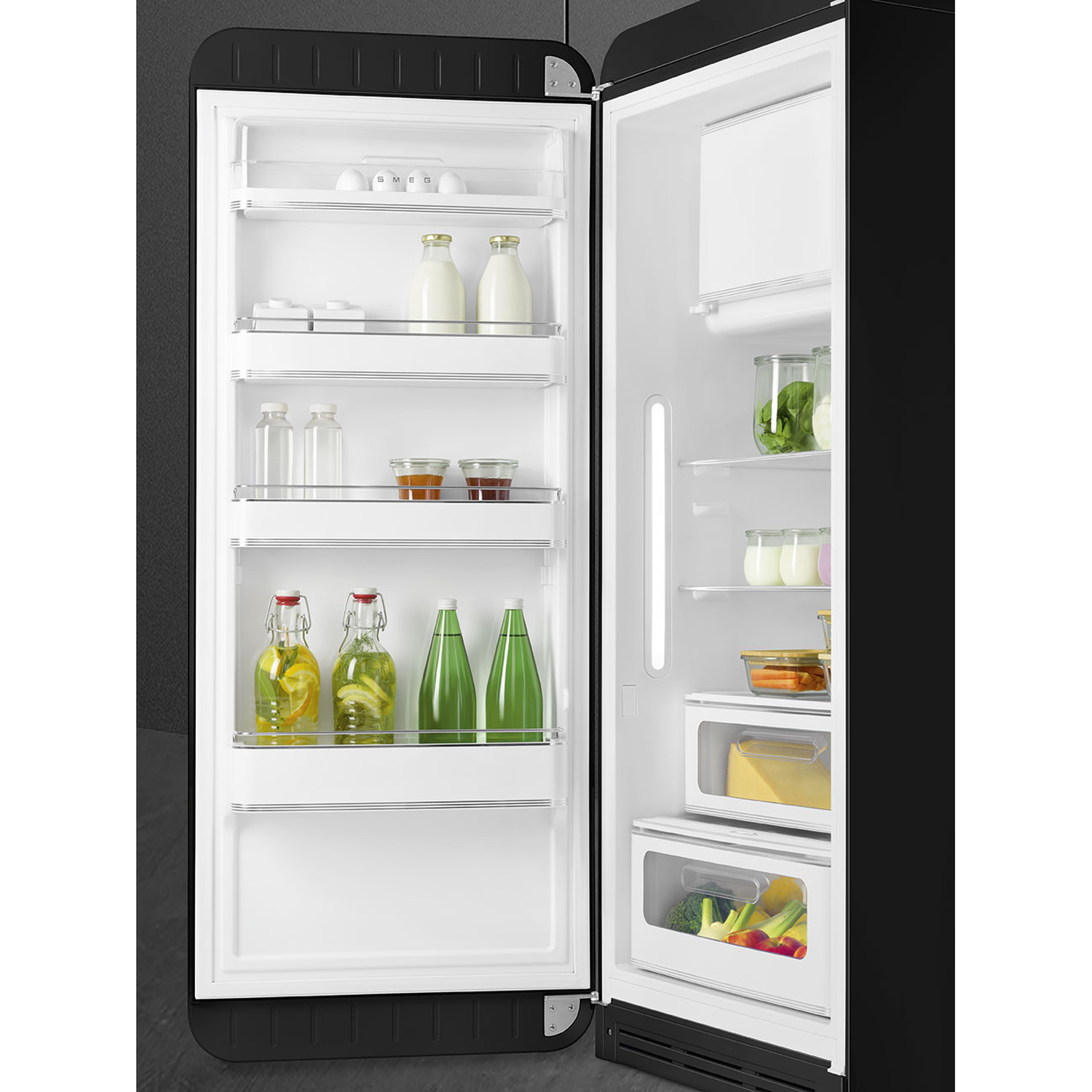 Open black refrigerator. Inside, shelves hold milk bottles, jars, and vegetables. Door has bottles of water and lemons.
