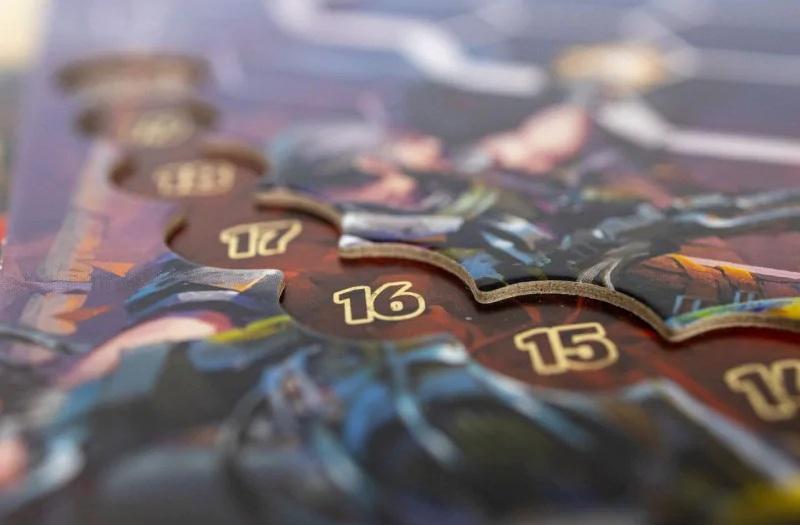 Zbliżenie elementów gry o numerach 15, 16 i 17. Elementy są brązowe ze złotymi numerami. Rozmyte tło sugeruje scenę fantasy.