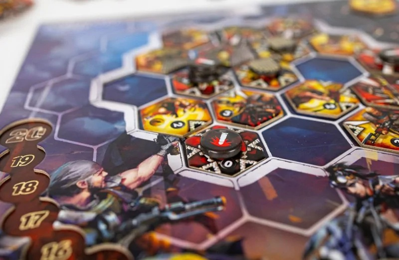 Gra planszowa z sześciokątnymi kafelkami, figurkami i czarnym żetonem. Figurki żołnierzy na planszy. Brązowe numery z boku.