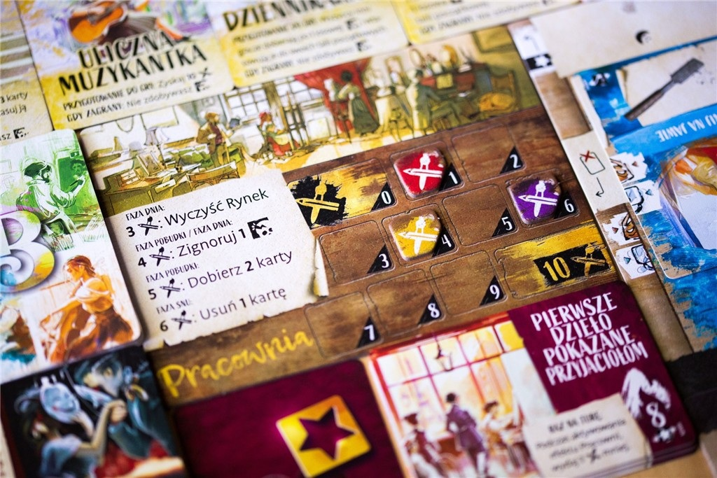 Szczegół gry planszowej z kartami, znacznikami i tekstem w języku polskim. Widoczne są różne elementy gry, w tym karty i fragmenty planszy.