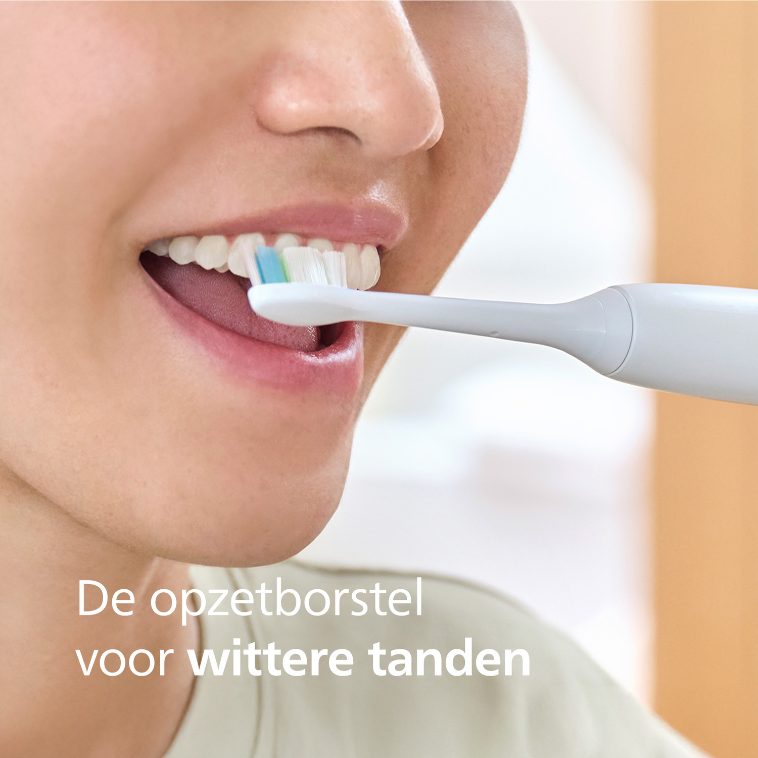 A person brushes their teeth with a white electric toothbrush. The brush has green and blue bristles. The person smiles.