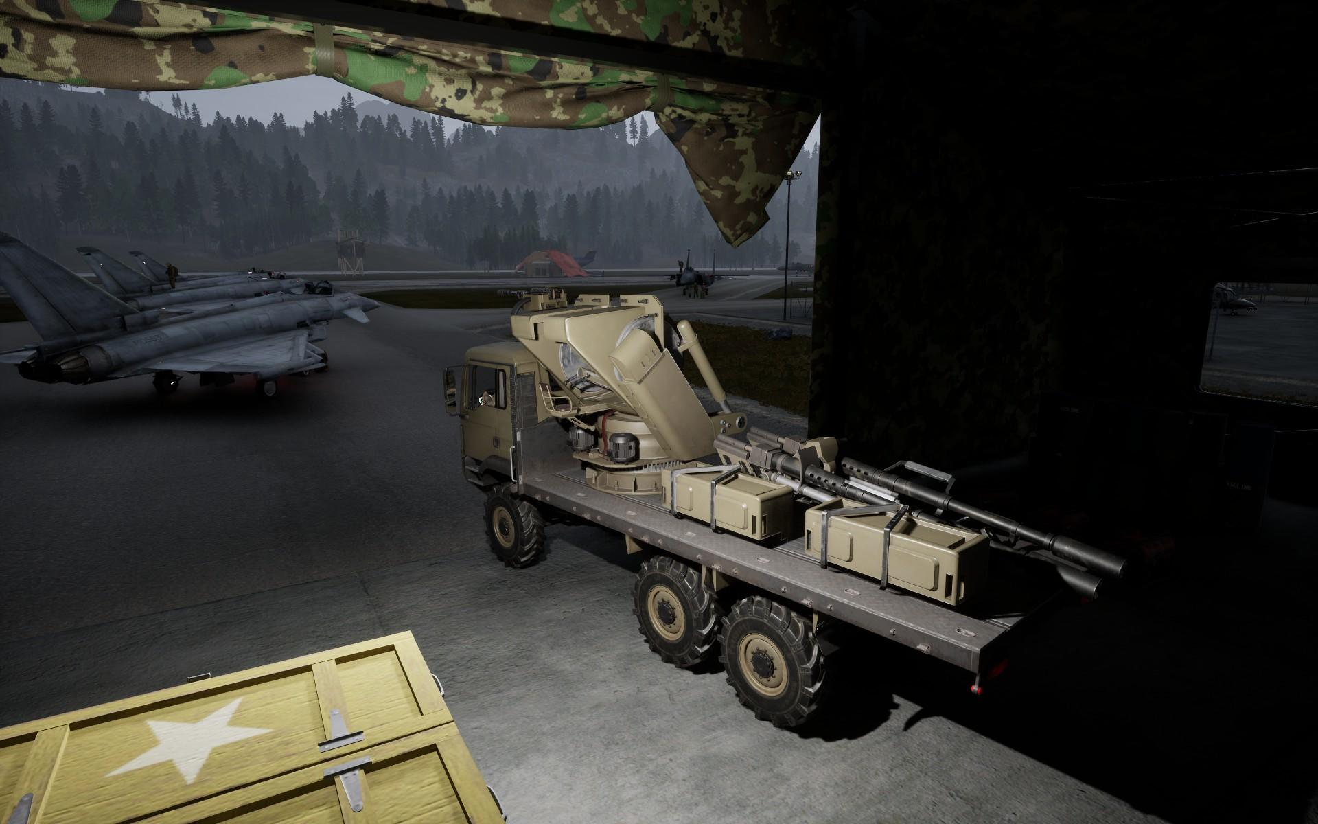 Militärfahrzeug mit großer Kanone, geparkt in der Nähe von Jets auf einem Flugplatz. Wald im Hintergrund, Tarnzelt über dem Kopf.