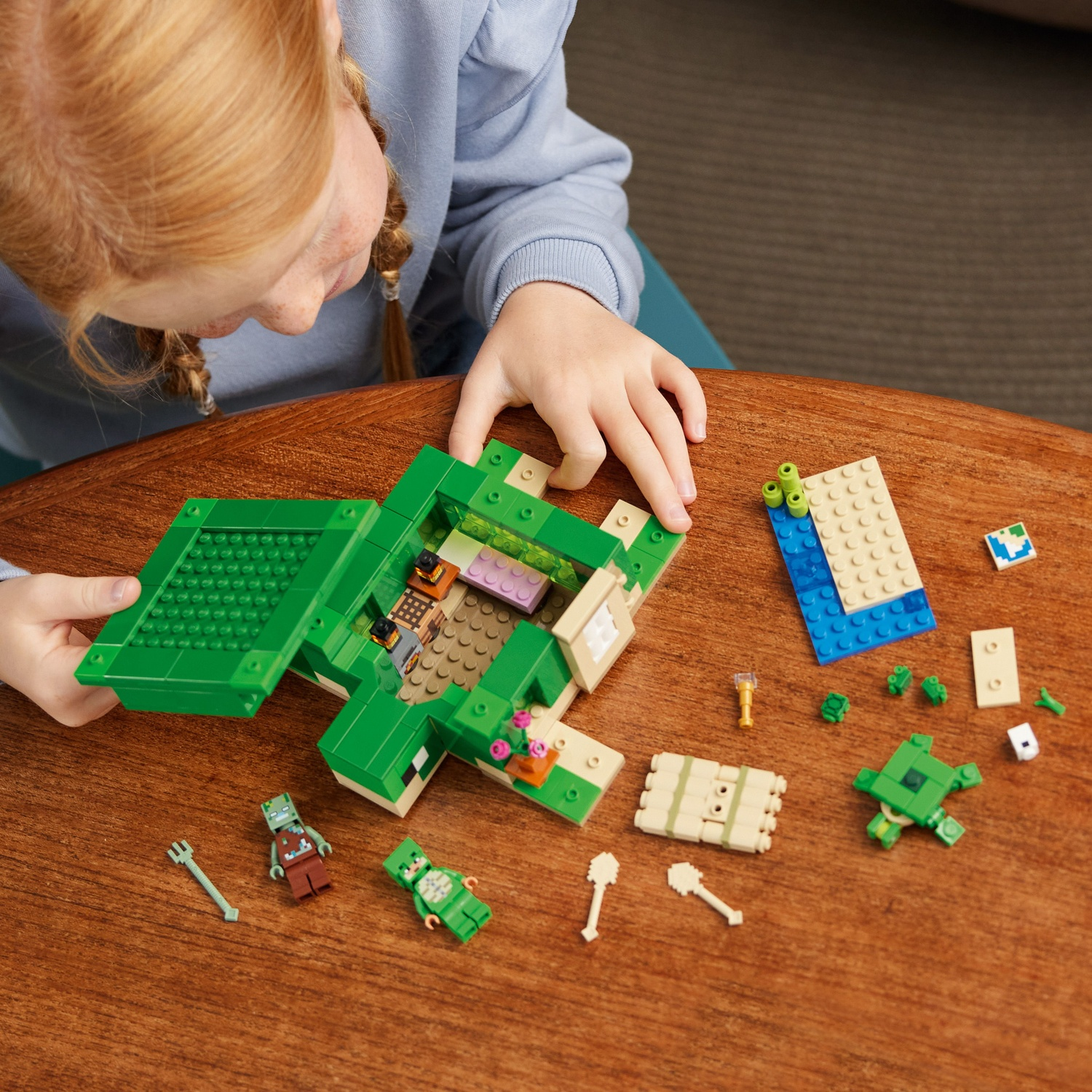Een kind speelt met een groene Lego-set op een houten tafel. Lego-blokken en figuren liggen verspreid. De handen van het kind zijn zichtbaar.