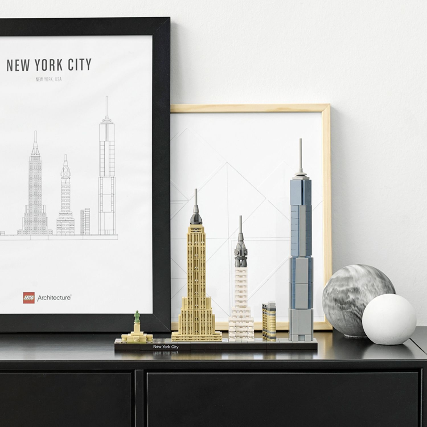 Un meuble noir avec des modèles Lego de New York et des imprimés encadrés. Comprend l'Empire State Building et d'autres monuments.