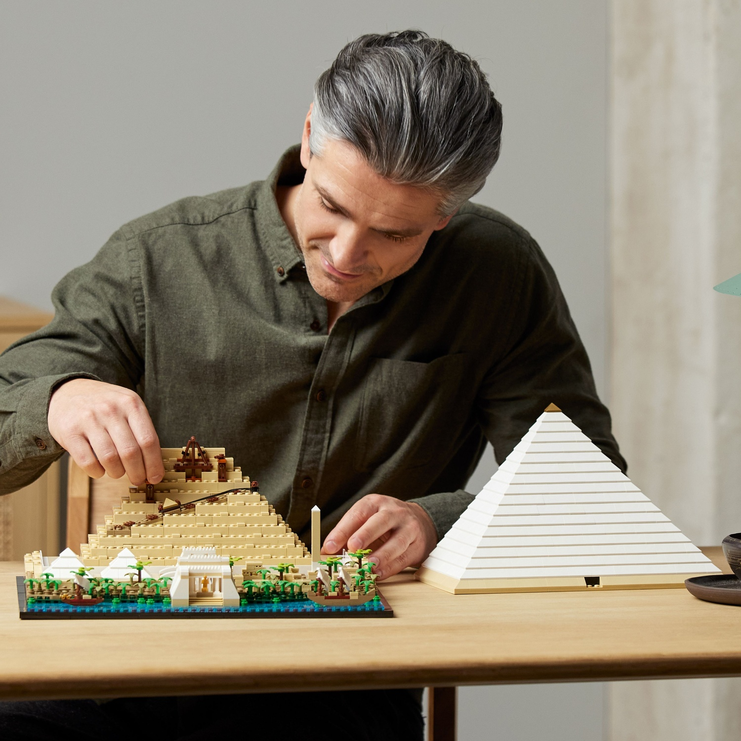 Een man bouwt een Lego piramide model op een houten tafel. Een voltooid piramide model staat ernaast. Details van de piramide.