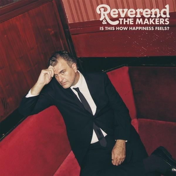 Mann im Anzug auf rotem Sofa. Er schaut in die Kamera. Text oben: "Reverend & The Makers" und "IS THIS HOW HAPPINESS FEELS?"
