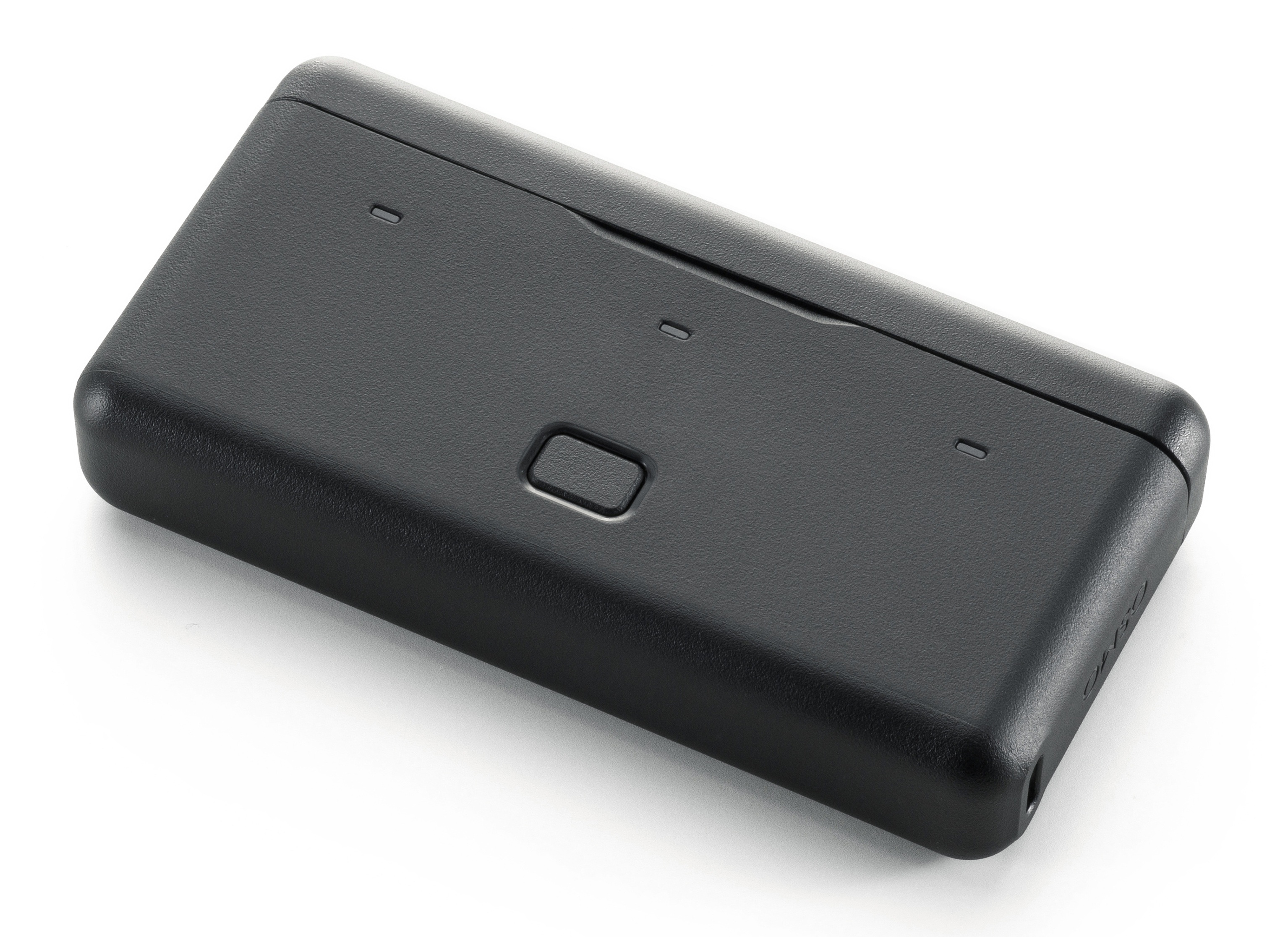 Czarne prostokątne urządzenie z zaokrąglonymi rogami. Ma małe wgłębienia i przycisk. Tło jest białe.