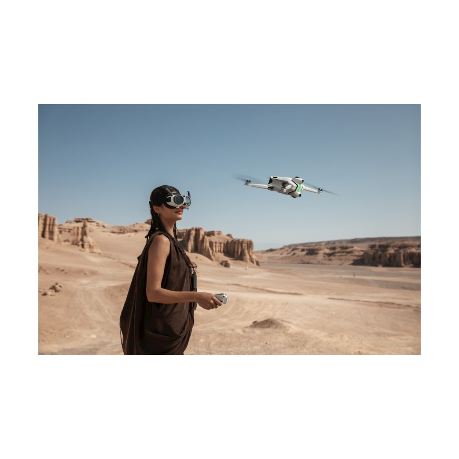 Una donna con occhiali controlla un drone su un paesaggio desertico. Il drone è in volo. Formazioni di sabbia e cielo blu sullo sfondo.