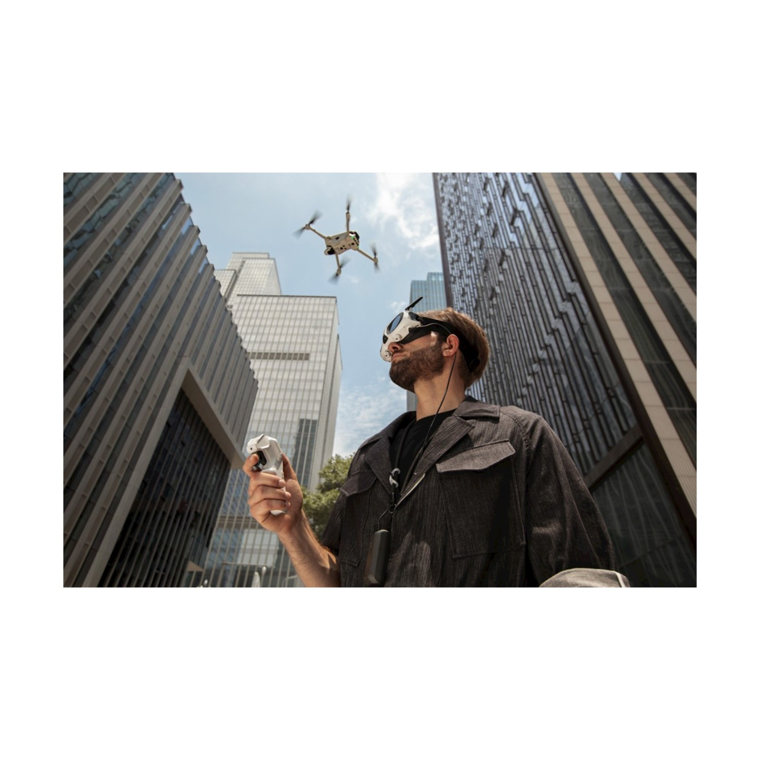 Un uomo con occhiali VR e un controller guarda un drone che vola nel cielo tra alti edifici.
