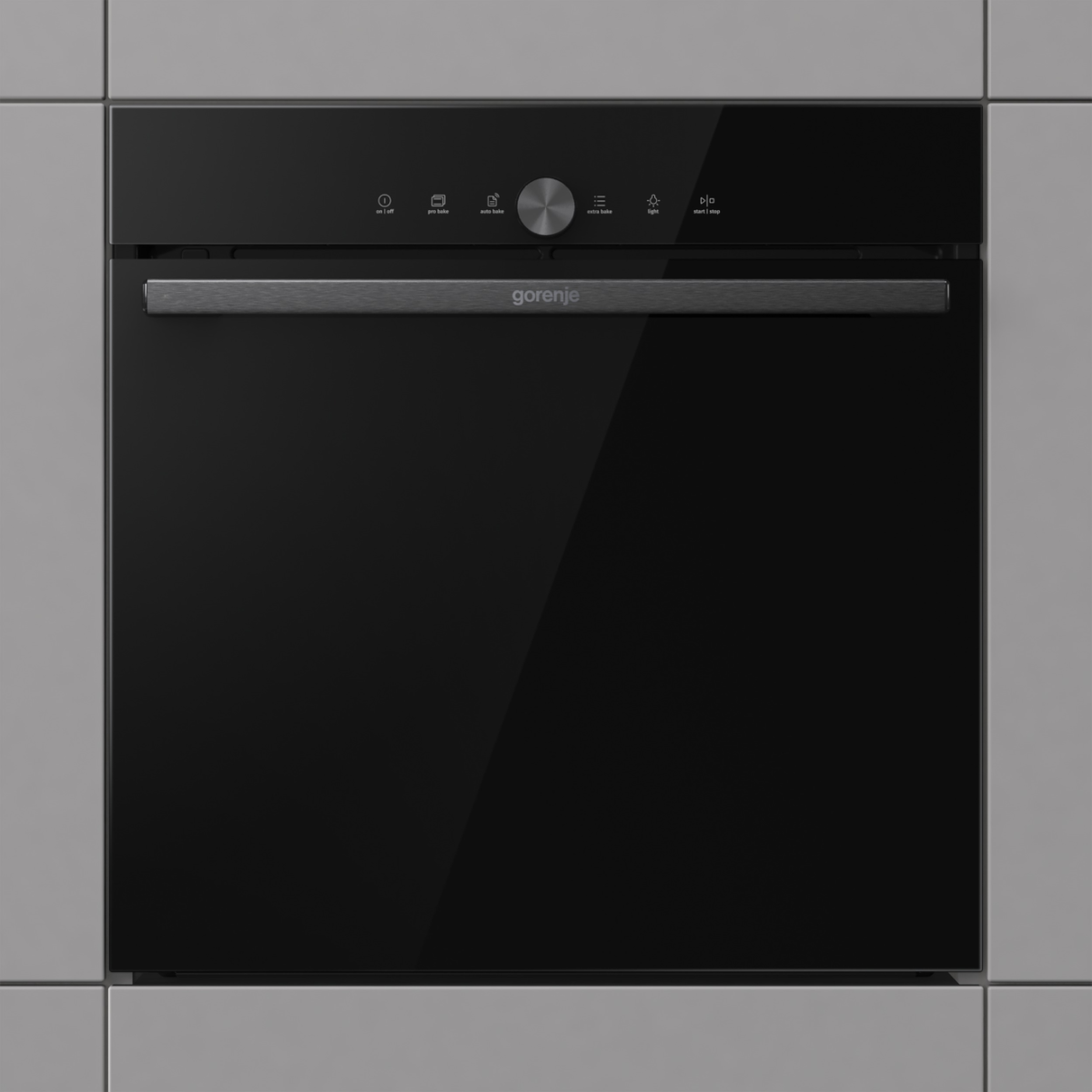 Egy fekete Gorenje sütő fogantyúval. A vezérlők az ajtó felett találhatók. A sütő egy szürke falba van beépítve.
