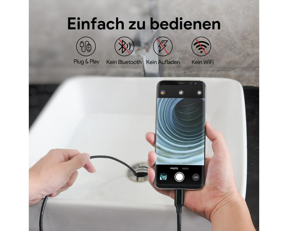 Egy személy egy csövek belsejét mutató telefont tart. A telefon egy kábelhez csatlakozik, a háttérben egy mosdókagyló látható.
