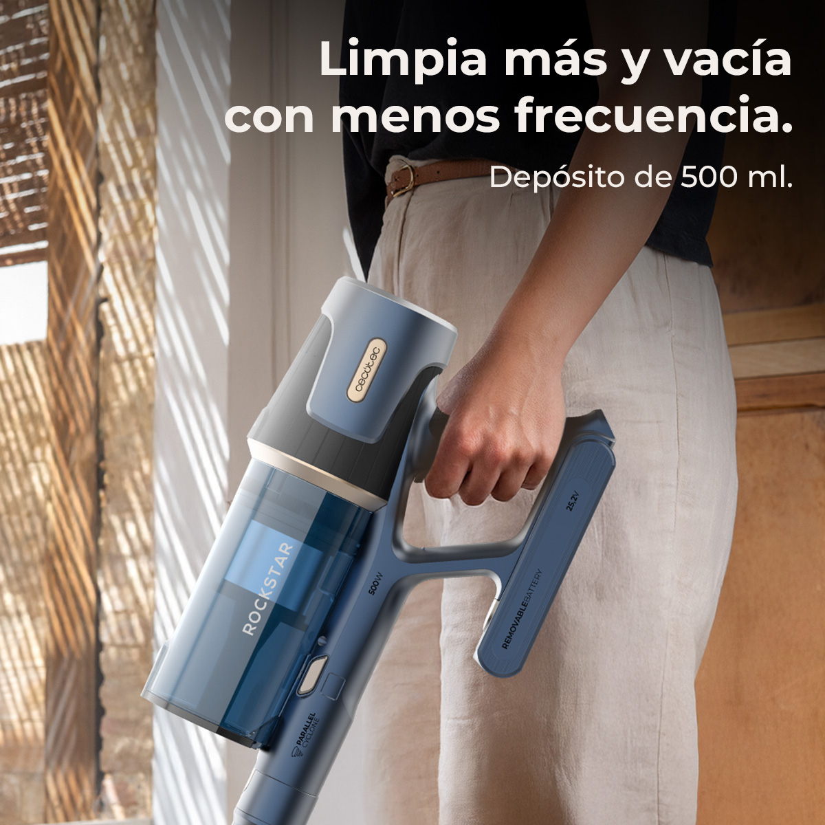 Una persona sostiene una aspiradora Cecotec Rockstar azul y gris. El texto dice: Limpia más y vacía con menos frecuencia. Depósito de 500 ml.
