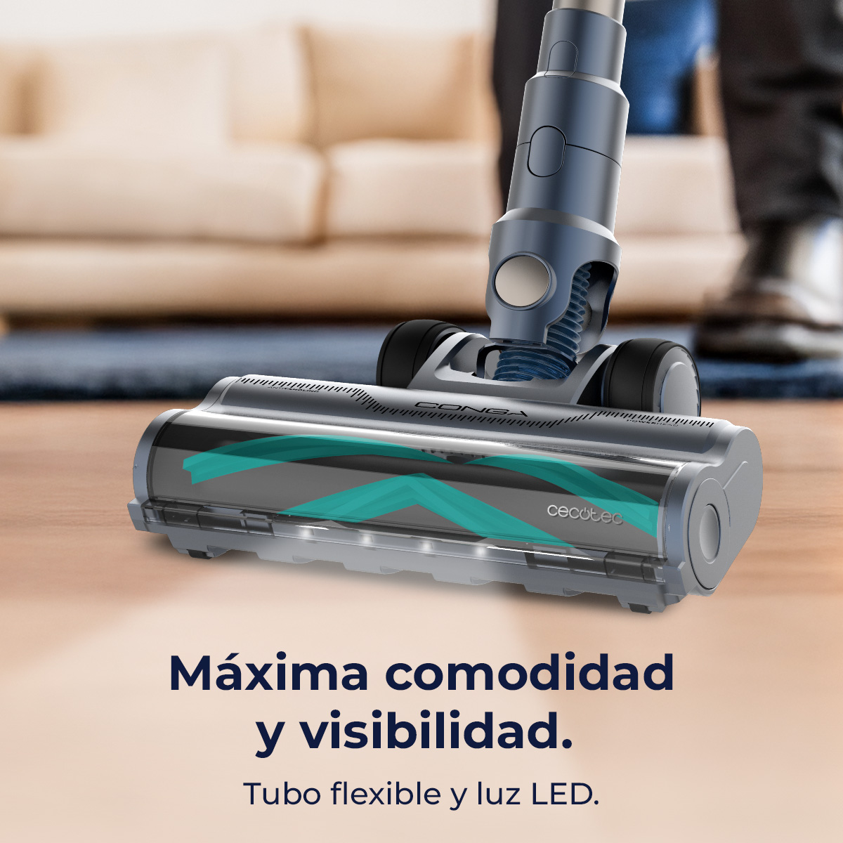 Primer plano de un cabezal de aspiradora azul y gris. El fondo muestra una habitación con un sofá y las piernas de una persona.